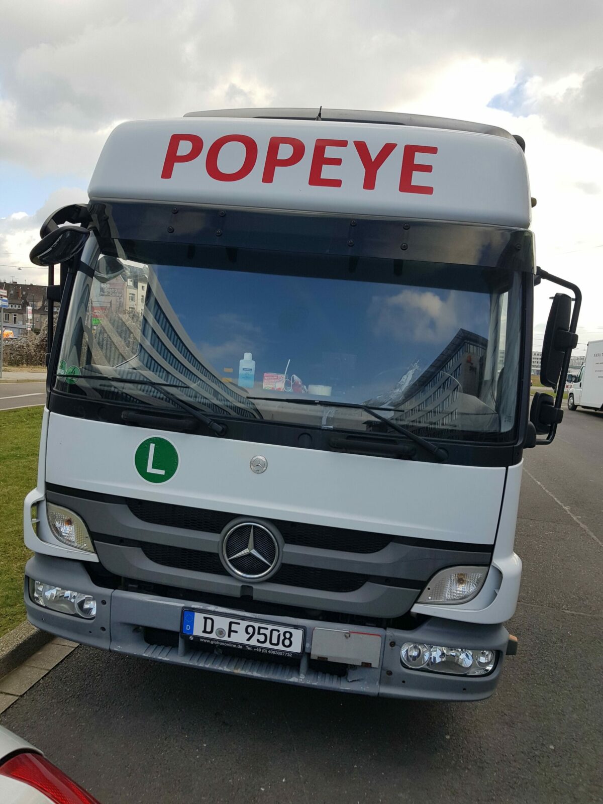 Weißer Mercedes-Benz-Lkw mit rotem Schriftzug "POPEYE" steht am Straßenrand.